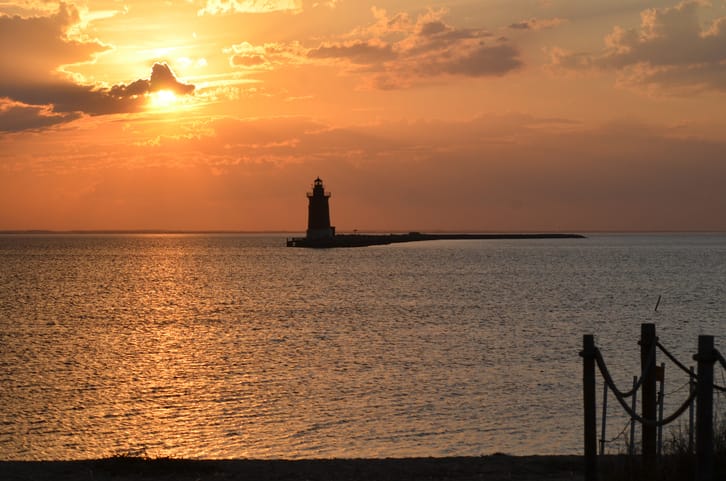 Delaware Breakwater Lighthouse at Cape Henlopen State Park at sunset with vibrant orange cloudscape and rope walkway